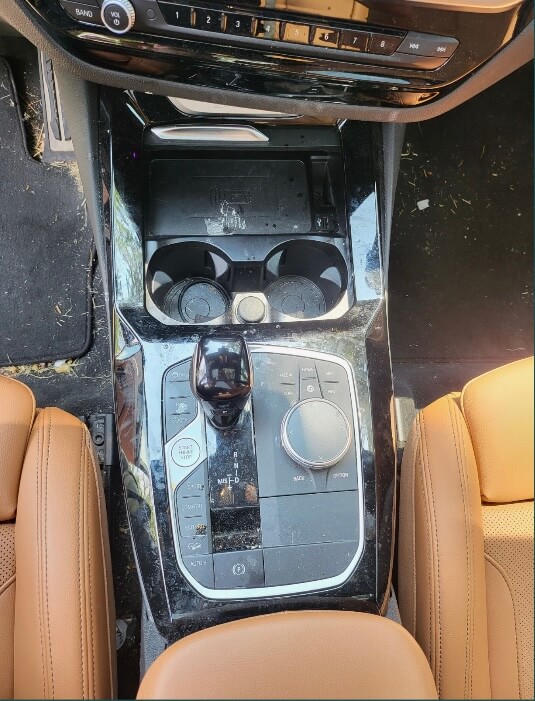 BMW interior before detailing with dirt and debris on the console, cup holders and floor mat