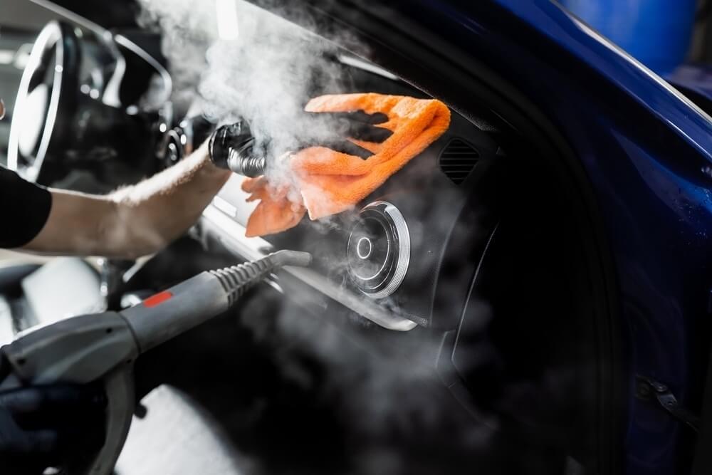 A technician steaming a dashboard and vents with an orange microfiber cloth
