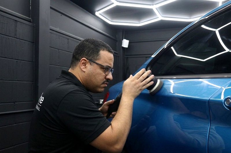 A technician machine-polishing a blue car door under hexagon studio lighting